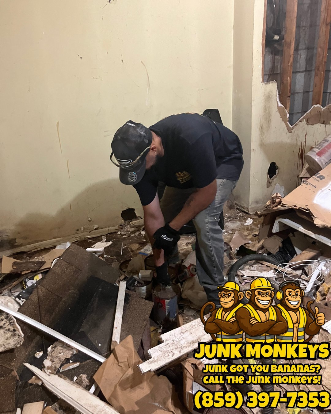 Worker in black shirt and welding mask sorting through debris in a demolished room with Junk Monkeys logo and contact number