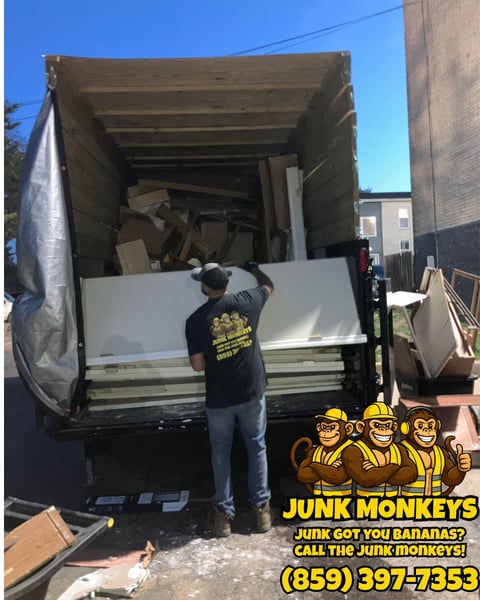 Worker loading white sheets into a junk removal truck with Junk Monkeys logo and contact number displayed