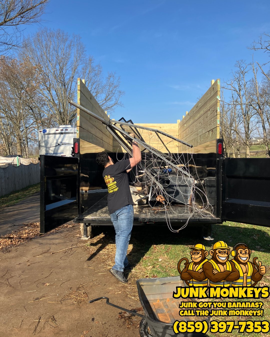 Worker loading branches into open utility trailer with yellow wooden sides on clear day