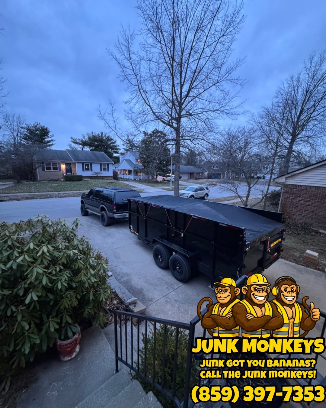 Black dump truck parked in suburban driveway with Junk Monkeys logo and phone number overlay