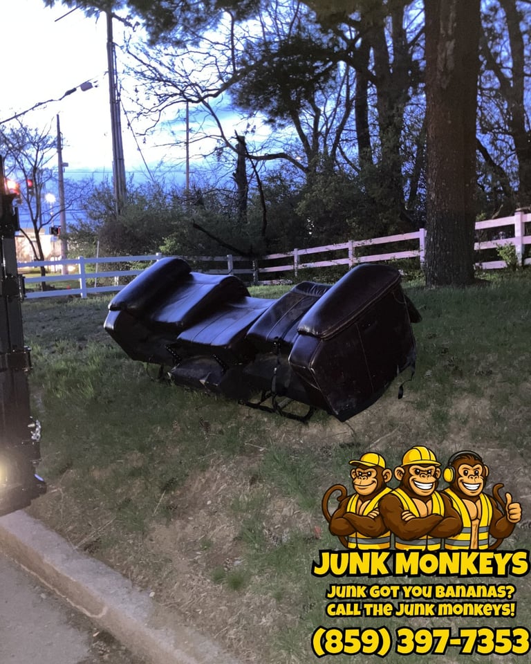 Three black leather saddles stacked on grass near white fence and trees with Junk Monkeys logo and phone number